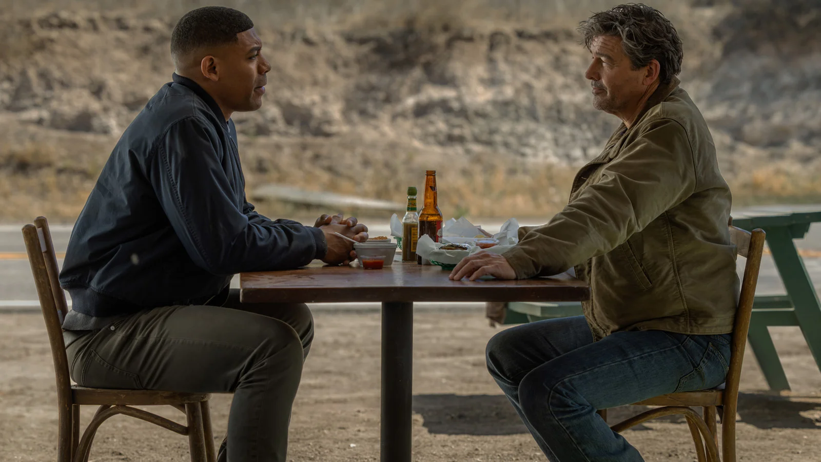 John Stewart and Hal Jordan sitting at a roadside table with food and drinks in Lanterns
