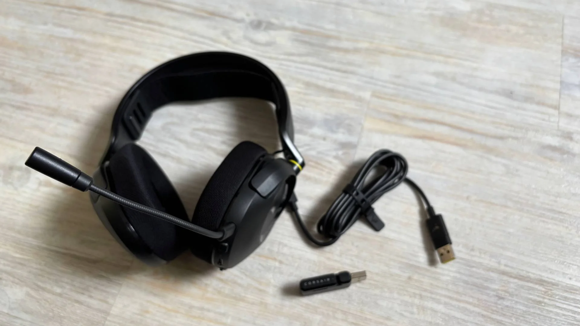 contents of the Corsair HS35 v3 headset box including the headset, mic, dongle, and USB C cable against a white hardwood floor background