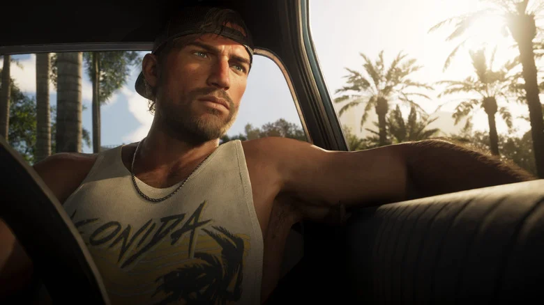 A man in the driver's seat of a vehicle, with bright sunlight and palm trees ion the background.