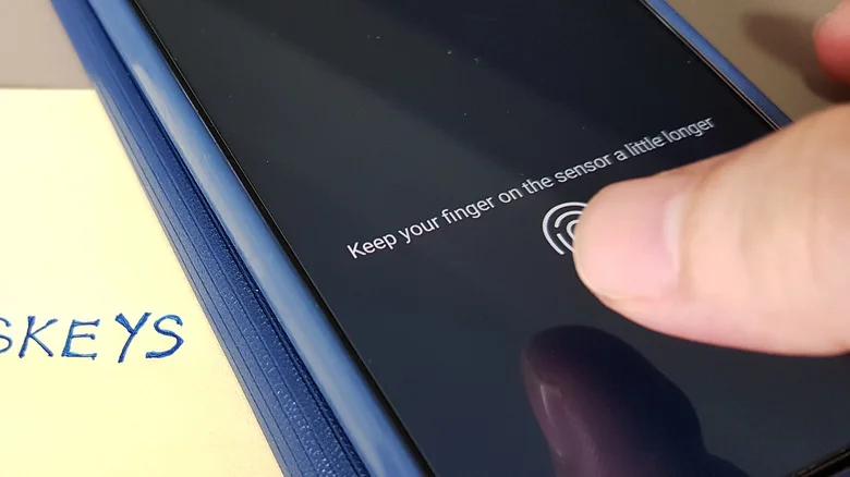 Finger being scanned on phone with a "passkeys" sticky note nearby.