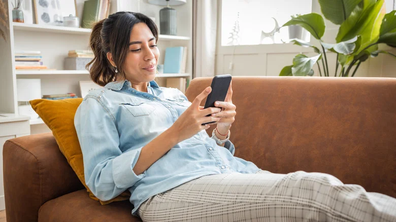 A woman using a smartphone while lying on a couch.